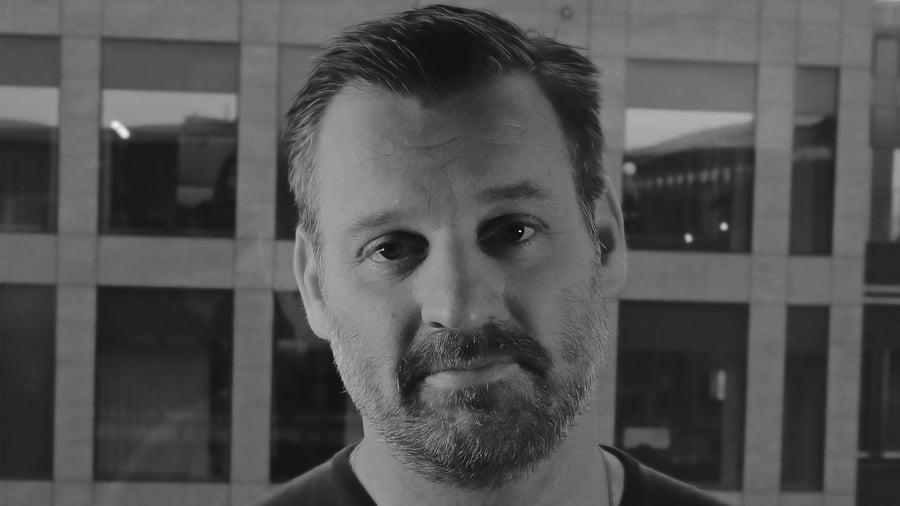 Porträttbild av Stefan Dufva tagen rakt framifrån med husfasad i bakgrunden.
